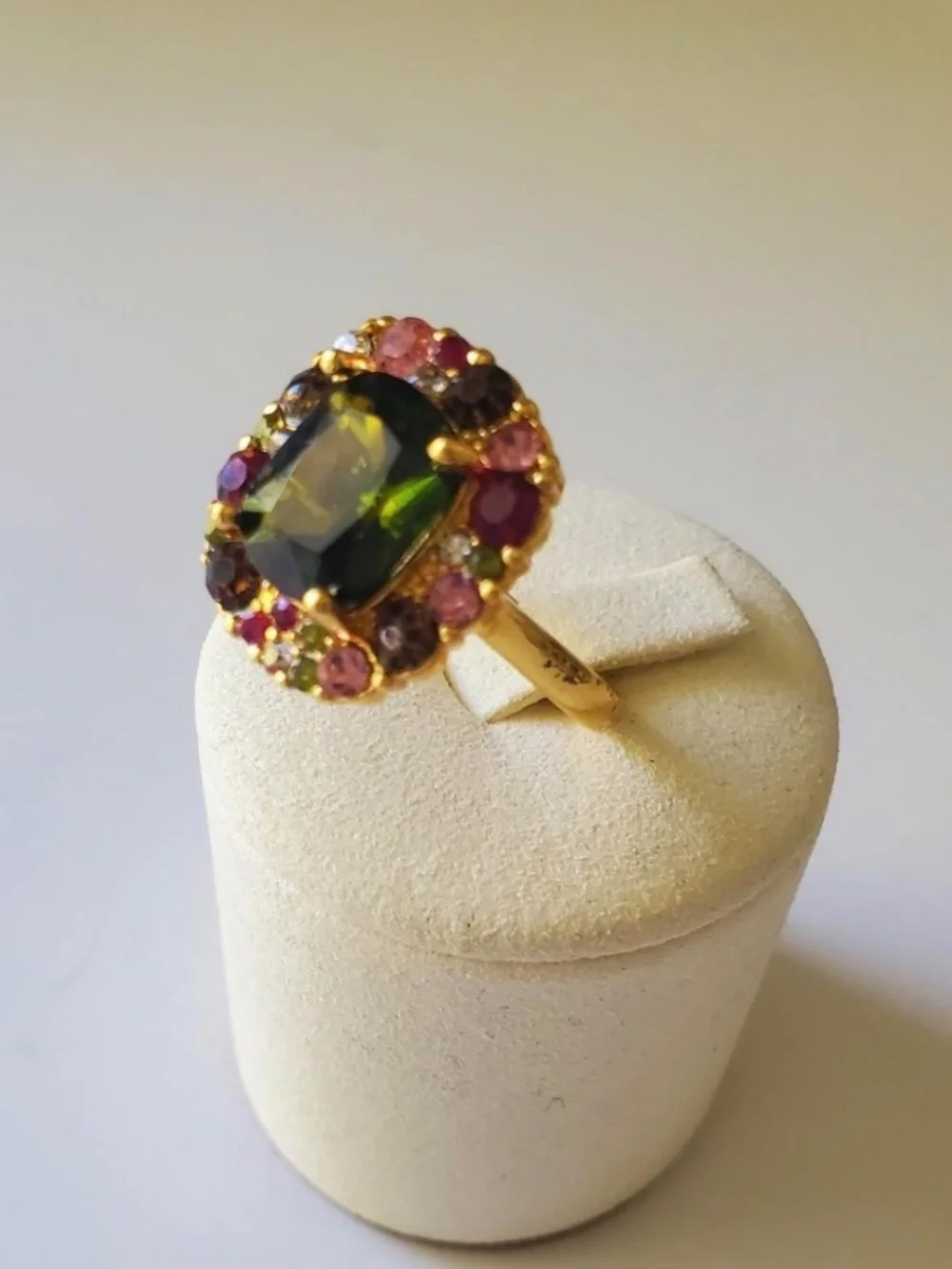 Gold ring with green central gemstone surrounded by pink and red rhinestones